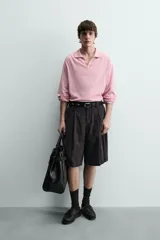 Bermuda negra de corte ancho (wide fit) confeccionada en tejido con mezcla de viscosa. Presenta pliegues en el delantero, bolsillos frontales y bolsillos de vivo en la parte trasera. Cierre frontal con cremallera y gancho metálico oculto.