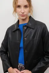 Chaqueta corta color beige con cuello de piel sintética negra, cierre frontal de botones y bolsillos laterales.