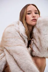 Campera de piel sintética en tono beige con textura suave y voluminosa. Presenta cuello alto, cierre frontal completo y mangas largas con puños amplios.