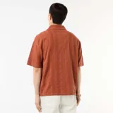 Camisa de manga corta confeccionada en tejido de punto fantasía de algodón, en tono marrón terracota. Cuenta con cuello solapa, abotonadura frontal y corte recto.