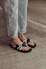 Sandalia tipo flip-flop con estampa cow print en blanco y negro. Presenta una tira ancha acolchonada que abraza el pie y una base negra lisa. Diseño liviano y cómodo de la marca Anne Chaussure.