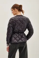 Campera acolchada de diseño matelassé con cierre frontal y cinturón ajustable con hebilla metálica. Presenta cuello redondo y mangas largas con puños elásticos.