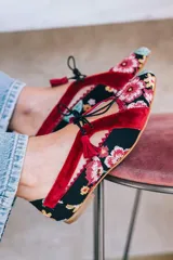 Zapatos tipo blucher de diseño artesanal, confeccionados en algodón con estampado floral multicolor sobre base negra. Presentan detalles en terciopelo color fresa, cierre con cordones rematados en borlas y suela de cuero.