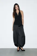 Top halter negro con escote drapeado tipo cascada y espalda descubierta. La prenda está adornada con pequeños apliques brillantes distribuidos por toda la tela y presenta un bajo asimétrico.