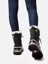 Botas de nieve Sorel modelo Caribou para mujer, de color negro con base de goma vulcanizada impermeable y detalles en blanco. Cuentan con parte superior de gamuza y nylon, cordones frontales con anillas metálicas y borde superior de pelo sintético blanco.