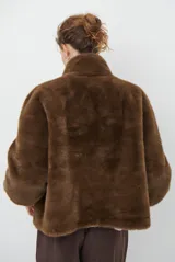 Chaqueta de piel sintética en color burdeos, con cuello alto y cierre frontal oculto. Presenta un diseño de corte recto y mangas largas con puños ligeramente ajustados.