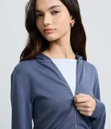 Campera corta con capucha fija, cierre frontal con cremallera y mangas largas, confeccionada en tejido modal con acabado satinado.