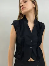Chaleco negro de lana con diseño estructurado, cuello alzado y detalle de alforzas verticales en los laterales. Presenta cierre frontal con botones metálicos y corte a la cintura.