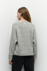 Sweater de tejido de punto color gris melange, con cuello redondo y diseño de franjas horizontales en relieve. Presenta mangas largas acampanadas y un corte holgado.
