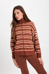 Campera de punto holgada con cuello tipo chomba y cierre frontal oculto. Presenta un diseño de rayas horizontales en tonos marrón, rojo y crema, con puños y ruedo acanalados. Incluye un parche bordado en la manga izquierda.
