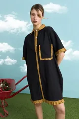 Túnica de algodón color negro, con cuello polo, manga corta, cartera frontal con botones y bolsillo ojal en el pecho. Presenta detalles de voladitos mostaza en el cuello, la botonera, los puños, el bolsillo y el ruedo.