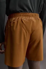 Pantalón corto deportivo color marrón oliva, confeccionado en tejido técnico ligero y elástico, con forro interior. Presenta cintura elástica ajustable con cordón, bolsillos frontales, bolsillo de seguridad trasero con cierre y aberturas laterales en el bajo.