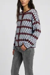 Saco tejido con cierre frontal de botones, cuello redondo y mangas largas. Presenta un diseño de patrón de rombos en tonos celeste y bordó.