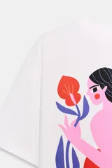 Remera blanca de corte oversize con cuello redondo y mangas cortas. Presenta un estampado artístico a color en el frente que ilustra una figura femenina estilizada con botas estilo western.