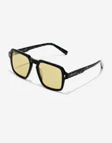 Lentes de sol Hawkers modelo Lash con armazón negro de frente cuadrado y patillas con estampado de mármol en tonos verdes. Presentan cristales amarillos y detalles metálicos en las esquinas.