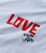 Remera boxy de algodón color celeste, con cuello redondo y mangas cortas. Presenta un estampado frontal con lettering y un estampado trasero grande con un corazón formado por círculos coloridos y una pequeña ilustración de una casa debajo, inspirado en la película "Up: Altas Aventuras".