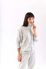 Conjunto de dos piezas confeccionado en tela plush, compuesto por una campera con cierre frontal y cuello alto, y un pantalón de corte recto. Presenta un diseño minimalista y cómodo en color gris claro.