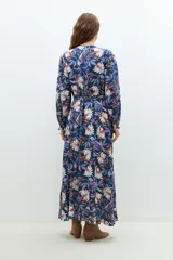 Maxi vestido azul marino con estampado floral en tonos blanco, rosa y azul. Diseño cruzado con lazo en la cintura y mangas largas.