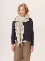 Bufanda o chal de lana color beige claro, con diseño de punto abierto calado en forma de rombos o espigas, y bordes ondulados.