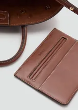 Cartera de mano color marrón, de diseño estructurado tipo trapecio, con doble asa corta y detalles de correas laterales ajustables con hebilla.