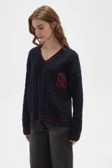 Sweater de tejido de punto con diseño de trenzas, cuello en V y detalles de rayas en contraste en cuello, puños y ruedo. Presenta un número bordado en el frente y tiene un corte holgado.