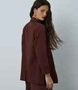 Blazer de sastrería color bordó, de corte oversized y largo, confeccionado en crepé. Presenta solapas clásicas, bolsillos frontales y detalle de pliegues en los puños.