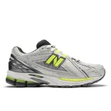 Championes New Balance modelo 1906R, color blanco y gris con detalles en amarillo neón y negro. Presentan una parte superior de malla perforada con superposiciones sintéticas, logo 'N' lateral en amarillo neón, y entresuela con tecnologías ABZORB SBS y N-ergy.