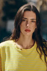 Camiseta amarilla con rayas horizontales blancas, cuello redondo amplio con detalle de botones decorativos a lo largo del escote y mangas cortas de corte holgado.