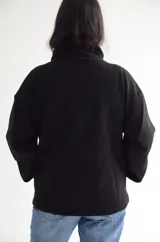 Abrigo negro de paño con diseño cruzado, cuello alto y cierre frontal con botones. Presenta una silueta estructurada y bolsillos laterales.