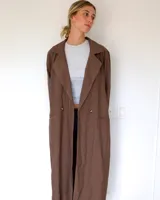 Trench largo de color marrón, con solapas amplias, cierre frontal de doble botonadura y bolsillos laterales.