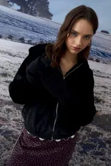 Chaqueta tipo teddy color negro, con capucha, cierre frontal metálico y puños tejidos.