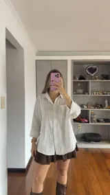 Camisa de corte oversize con estampado de rayas verticales finas, cuello clásico, cierre frontal con botones y bolsillo en el pecho.