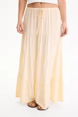 Pollera larga de viscosa color beige, con elástico y cordón ajustable en la cintura, y diseño escalonado acampanado.