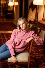 Blusa rosa de algodón con cuello alto y mangas largas abullonadas. Presenta detalles de cinta negra en el cuello y los puños, hombros con diseño princesa y cierre de lágrima con botón forrado en la parte posterior del cuello.