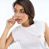 Musculosa blanca de punto con diseño de corazón bordado en hilo dorado en el pecho, cuello redondo y hombros ligeramente estructurados.