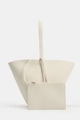 Bolso de hombro de piel en color blanco, con diseño tipo bucket, asa fija y detalle de tira colgante con nudo en el lateral.