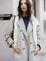 Trench coat largo color beige con doble botonadura, cinturón ajustable y bolsillos laterales.