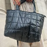 Bolso tote negro con diseño acolchado y cierre de cremallera. Tiene dos asas de hombro y un bolsillo frontal con cierre.
