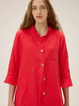 Camisa de lino de silueta relajada y largo irregular, color beige, con cuello mao, botones frontales a contratono y mangas tres cuartos terminadas en volados.