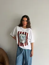 Remerón de algodón blanco con corte oversize y cuello redondo, que presenta un estampado frontal con diseño de una lata de sardinas sobre fondo de rayas.