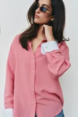 Camisa de rayas finas color rosado, con cuello solapa y puños largos en color blanco a contraste. Presenta cierre frontal con botones y bajo asimétrico con aberturas laterales.