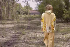 Canguro con capucha y cierre frontal, color beige con estampado de hojas en tonos marrones y amarillos. Mangas largas en color gris.