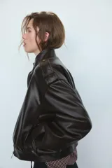 Cazadora de cuero sintético con cuello subido, manga larga con puños y trabillas en los hombros. Presenta un diseño abullonado en la cintura, bolsillos laterales y cierre frontal con cremallera y botones a presión ocultos. Posee un acabado efecto lavado y forro interior a tono.