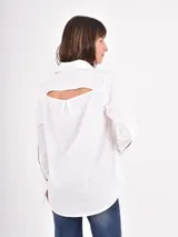 Camisa blanca de corte clásico con cuello camisero y puños anchos destacados. Presenta cierre frontal oculto por tapeta y dobladillo redondeado.