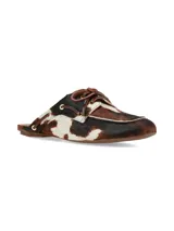 Zuecos Arno destalonados confeccionados en cuero con pelo con estampado animal print tipo vaca en tonos marrones, negros y blancos. Presentan diseño de inspiración náutica con cordones de cuero cruzados y ojalillos metálicos dorados.