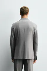 Blazer slim fit de color gris, confeccionada en tejido con lana. Presenta cuello con solapas de muesca, cierre frontal con un botón, bolsillos de solapa en la cadera y bolsillo de vivo en el pecho.