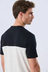Remera de algodón y poliéster de corte clásico, con diseño en bloques de color negro en la parte superior y gris melange en la inferior. Presenta cuello redondo, mangas cortas y un pequeño estampado tipográfico en el pecho.