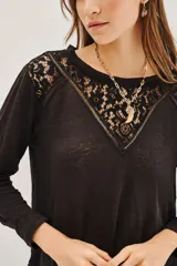 Remera de manga larga color negro, con detalle de encaje en la parte superior delantera y hombros. Presenta un corte holgado y fluido.