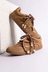Zapatillas urbanas de gamuza color marrón, con diseño de cordones decorados con cuentas de piedra y detalles de líneas brillantes en los laterales. Presentan suela de goma texturizada al tono.