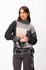 Sweater de punto con diseño patchwork en tonos gris, grafito y crudo, con cuello alto tejido. Presenta una estructura de bloques de color y texturas variadas, incluyendo detalles de trenzas y tejido acanalado.